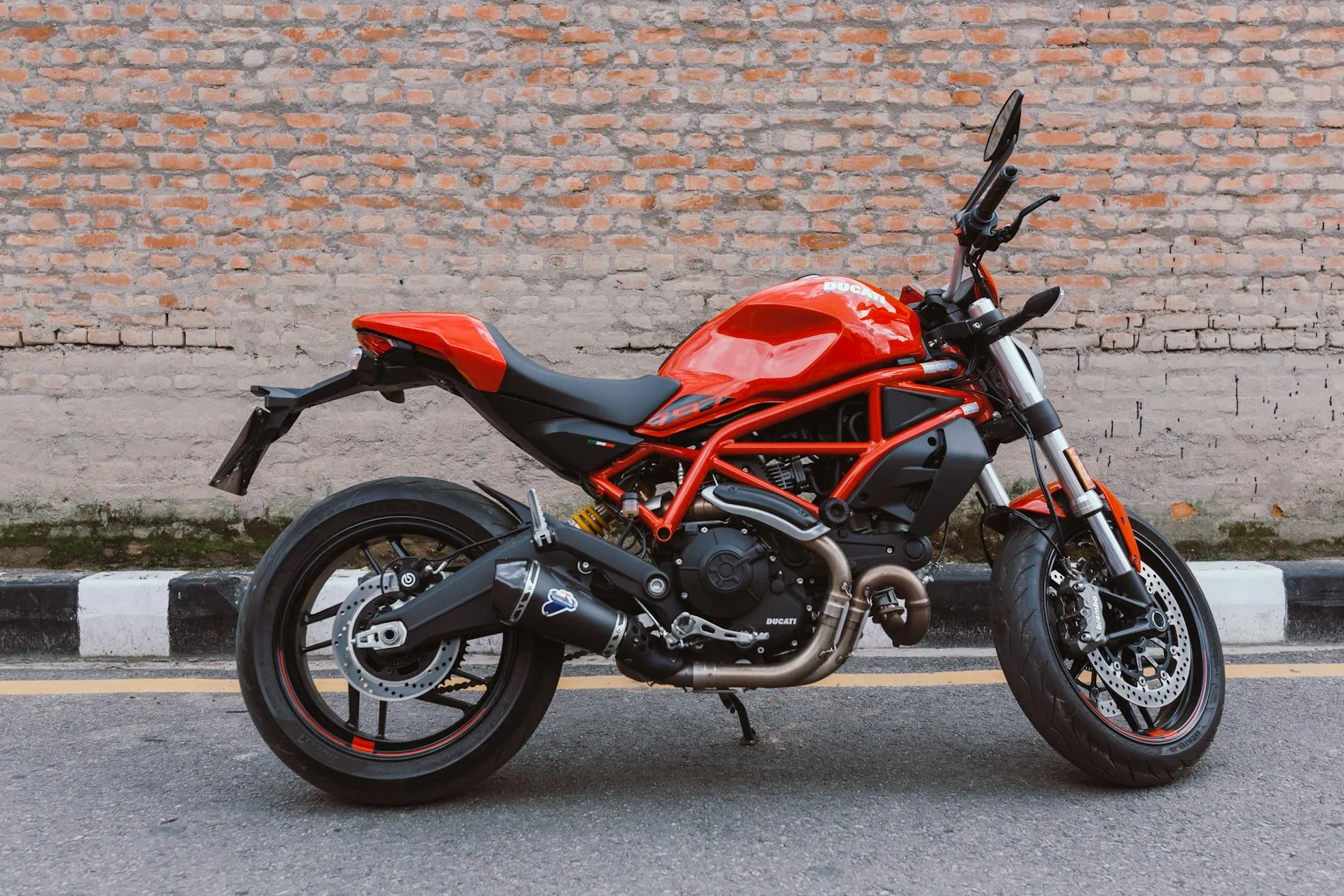 A red Ducati Monster parked in front of a brick wall
